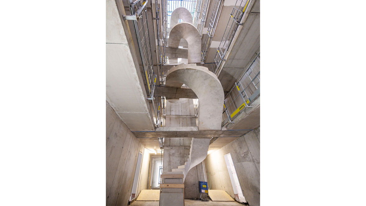 Von den Außenwänden des Lichthofs spannen dabei Stege, die von den Galerien erreichbar sind. Über jeweils einen Steg wird die zentral hängende, halbgewendelte Stahlbetontreppe in den Geschossen bedient.